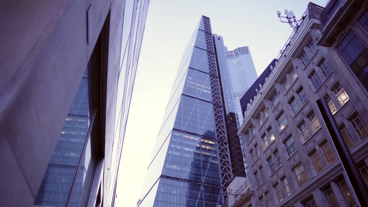 Looking up at London skyscrapers downtown at dusk, clear sky and building lights with reflections, smooth city reveal