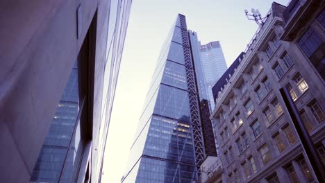 looking up at london skyscrapers downtown at dusk, clear sky and building lights with reflections, smooth city reveal