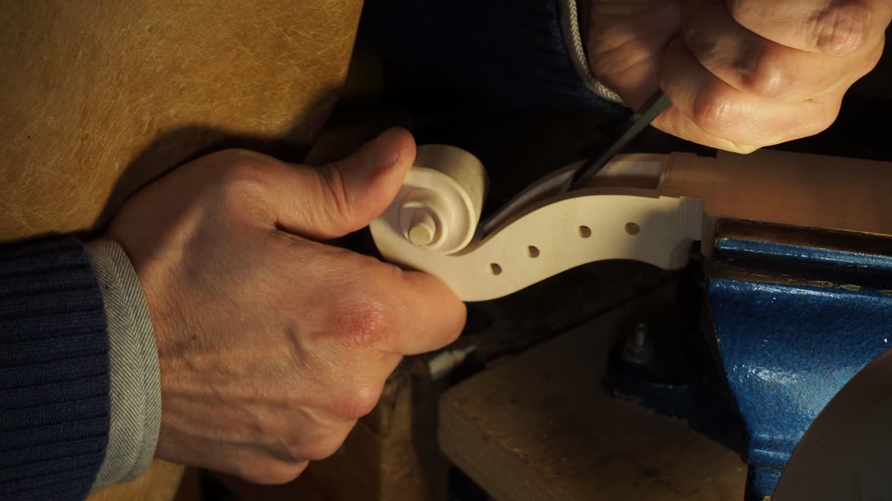 Extreme close-up of a luthier’s hands carving the volute and peg box of a new violin in the Cremonese tradition, highlighting fine detail and technique
