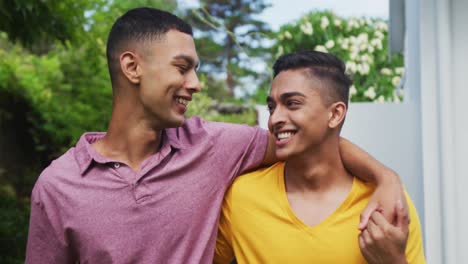 smiling mixed race gay male couple walking in garden hugging and kissing