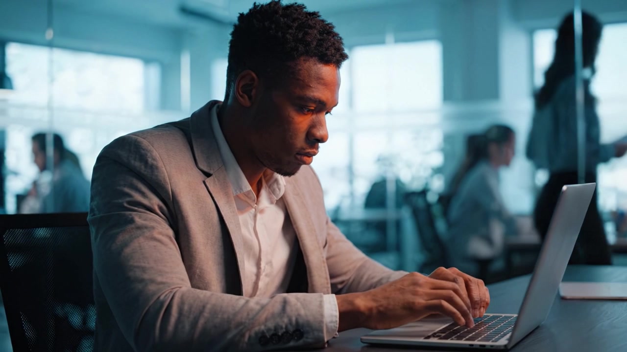 Focused Professional Working on Laptop in Modern Office Environment During Daytime, Engaged in Tasks Requiring Concentration and Skillful Keyboarding Abilities.