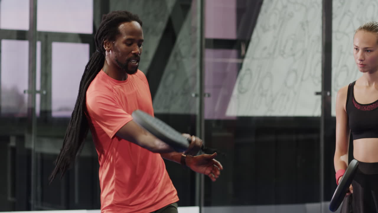 Young woman practicing padel tennis swing with coach in modern indoor court