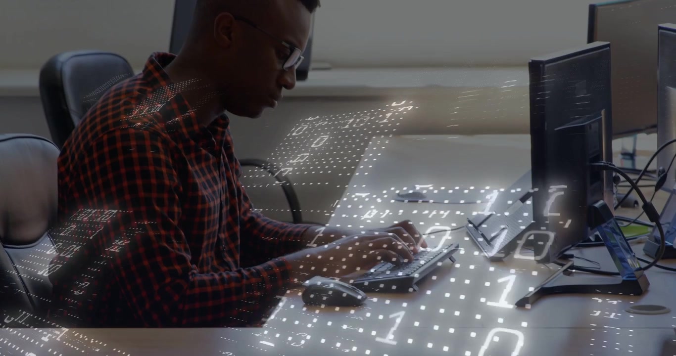 Man typing in office, initiating digital binary overlay across keyboard and monitor while coding