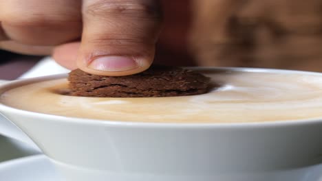 una mano sumergiendo una galleta de chispas de chocolate en una taza de capuchino