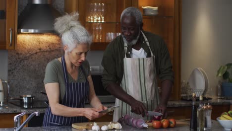 Una-Pareja-Enferma-De-Raza-Mixta-Con-Delantales-Cortando-Verduras-Juntos-En-La-Cocina-De-Casa