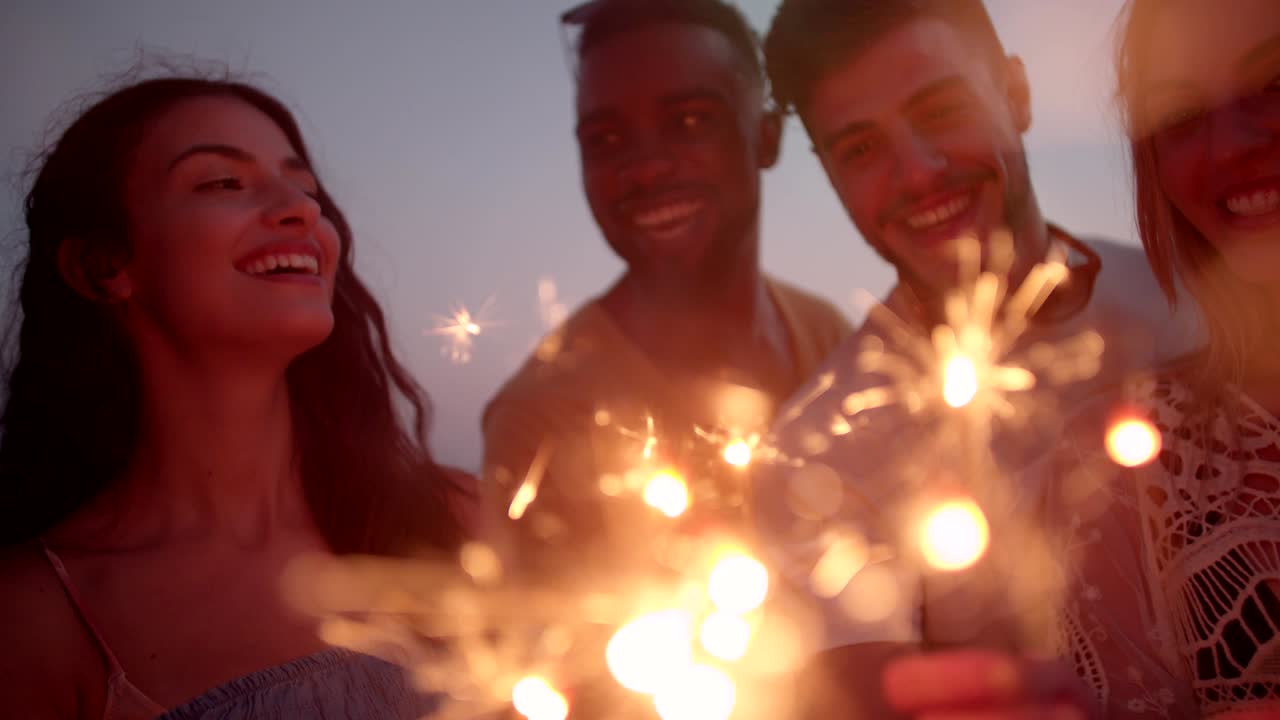 jóvenes hipsters multiétnicos celebrando con chispas en la fiesta de playa de verano