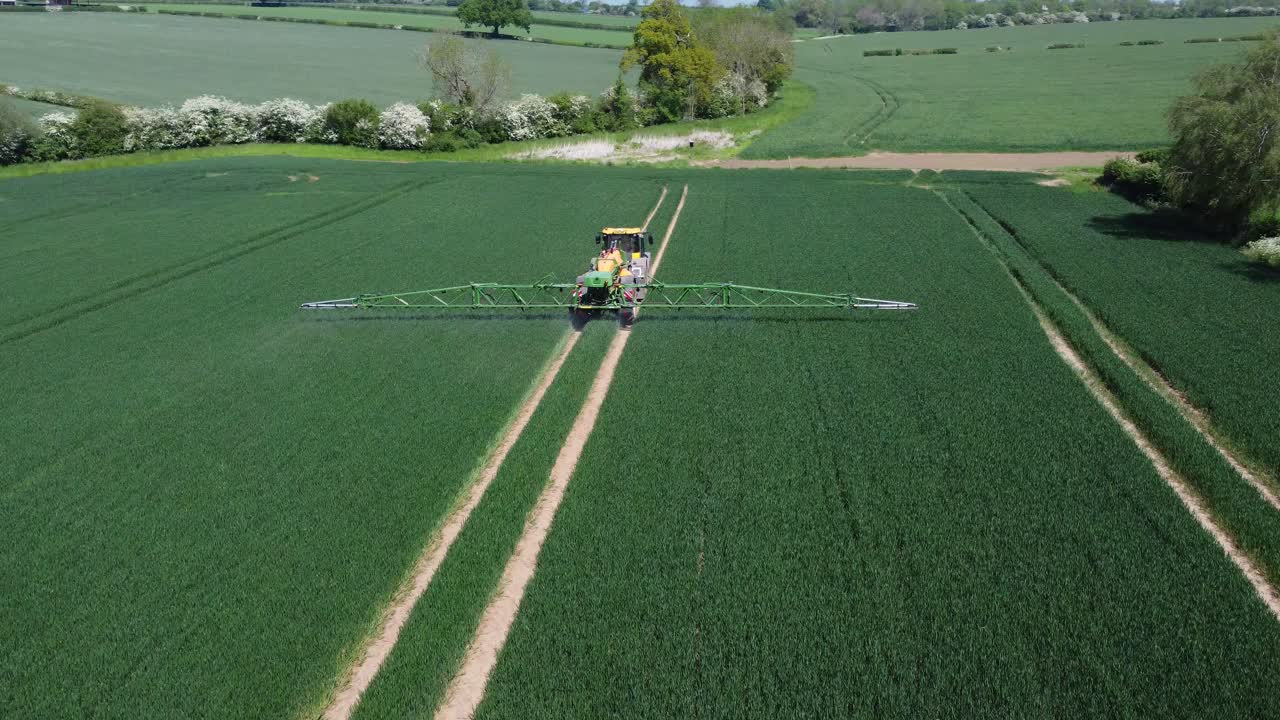 un tiro cercano de un tractor verde y amarillo rociando sus cultivos mientras trabajan sus campos