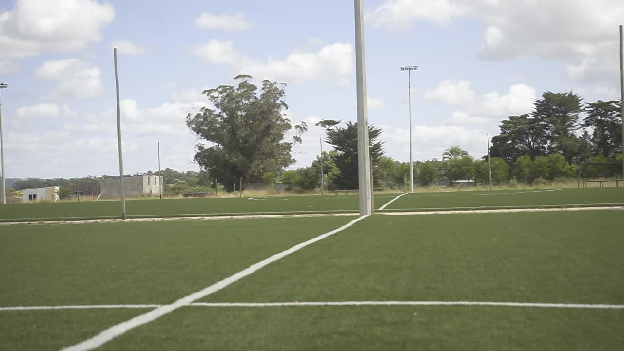 Verdant soccer pitch displaying crisp white boundary lines under bright sunny sky with soft cloud formations spreading across open landscape