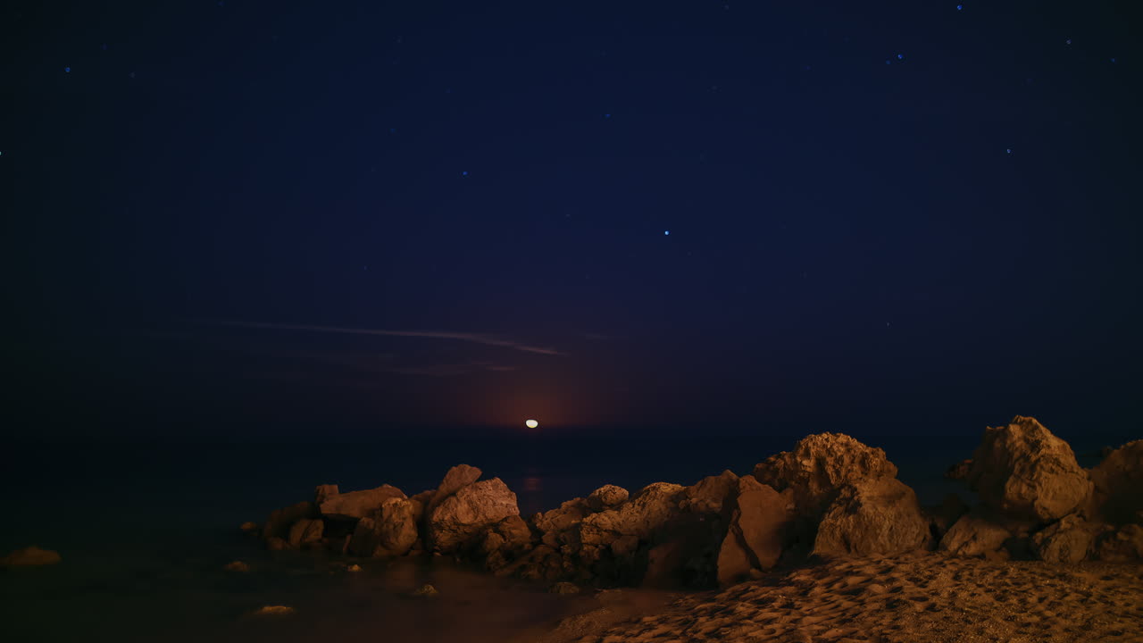 Video timelapse 4K: Luna epica che sorge sul mare, con scia lunare, stelle e meteoriti che cadono