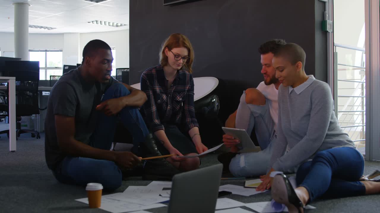 Front view of Young cool mixed-race business team planning and sitting on floor of modern office 4k