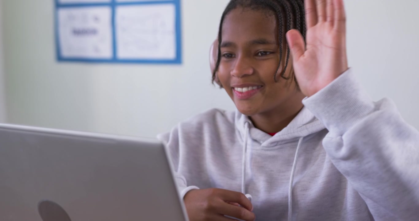 Adolescente na Mesa com Laptop e Fone de Ouvido Rosa, Ouvindo Após Ser Cumprimentado e Acenando