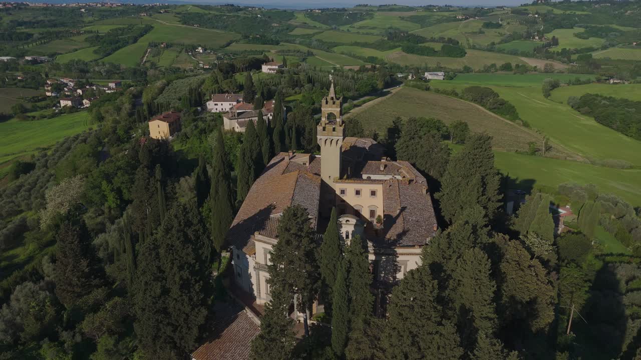 Drone orbit around Castello di Montegufoni in Tuscany. Surrounded by cypress trees and vineyards, the historic castle is bathed in golden morning light with a wide view of the Tuscan countryside.
