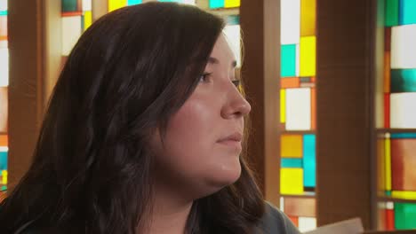 Extreme-close-up-of-a-pretty-young-ethnic-female-staring-sadly-at-the-altar-inside-a-church-sanctuary-while-sitting-in-a-pew