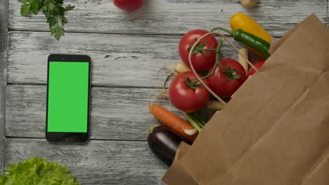 tomato rolling near vegetables and smartphone