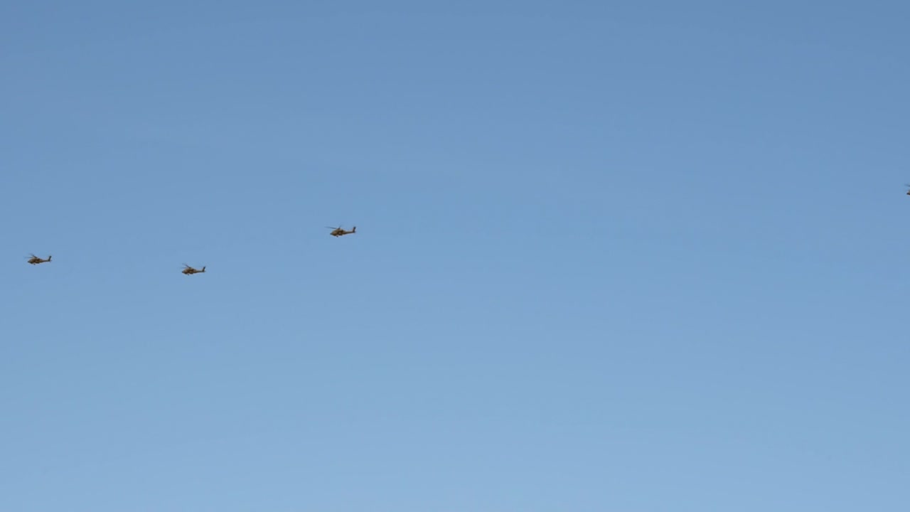 At a distance, a black helicopter formation leads a Chinook helicopter over the Sonoran Desert.