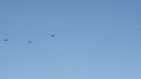 at a distance, a black helicopter formation leads a chinook helicopter over the sonoran desert.