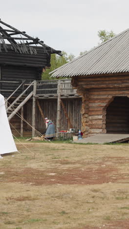 medieval courtyard with wooden arch above gate and white tent on cloudy day. people have lunch sitting on benches at table near stairs to observation deck