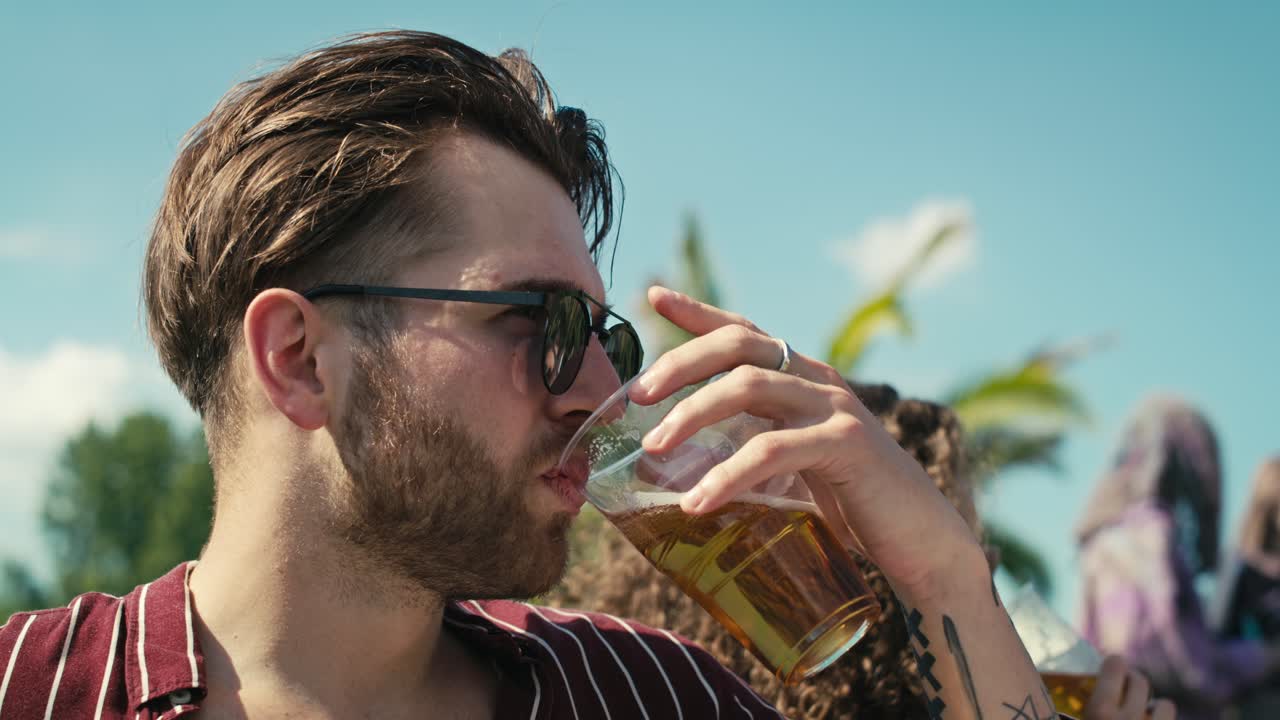 Close up of young caucasian man drinking beer from disposable cup at music festival and looking around