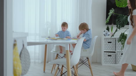 young mom and two sons 2-4 years old draw pencils drawing on boomega sitting at the living room table in slow motion