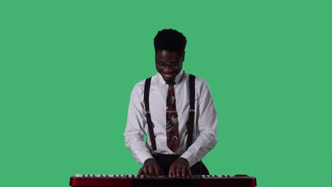 portrait of young african american man smiling and playing a fast melody on a keyboard synthesizer. black male with tie and glasses in white shirt posing on green screen in studio. close up