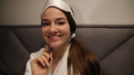 Attractive-model-posing-with-a-sleeping-mask-and-hair-tie-while-wearing-a-robe-sitting-in-bed