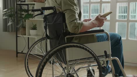 asian man sitting in a wheelchair reading book near door in the house
