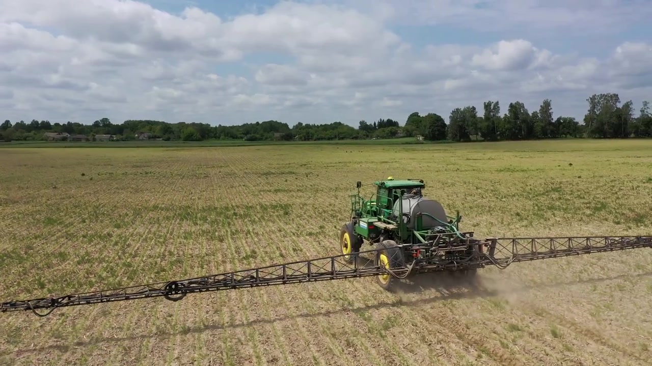Trattore agricolo che irrora fertilizzante su un vasto campo