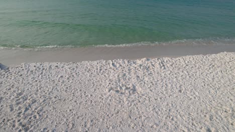 pan of white sand beach with clear emerald waters on a summer day