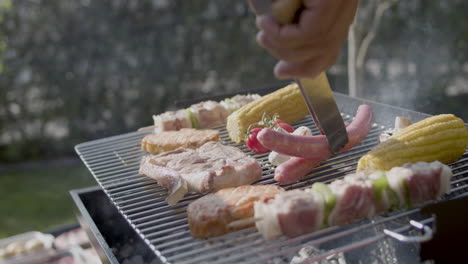 close-up of male hand turning over sausages on barbeque grill