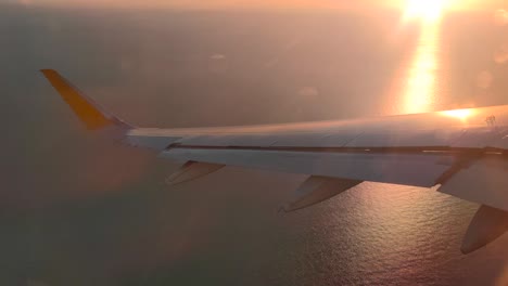 backlight of an airplane wing at sunset while the plane maneuvers over the sea