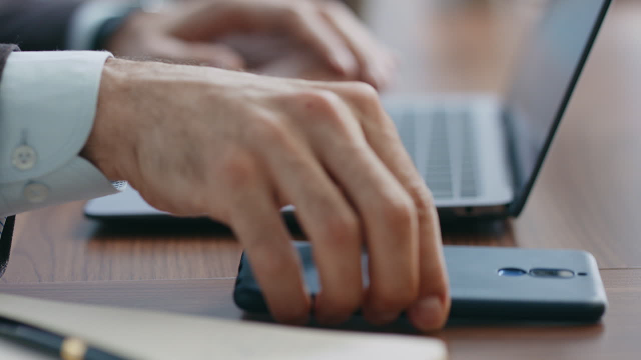 Closeup man hands typing laptop keyboard taking smartphone from office desk.