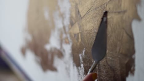 Unrecognizable-person-drawing-with-spatula.-The-hand-of-a-woman-artist,-holding-a-spatula-for-drawing-and-applying-paint-to-the-canvas.-Close-up-footage