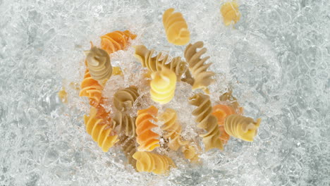 colorful fusilli pasta falling into pot of boiling water making a splash in slow motion, table top view
