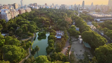 Dolly-in-flying-over-natural-reservoir-park-surrounded-by-Palermo-neighborhood-buildings-at-sunset,-Buenos-Aires,-Argentina