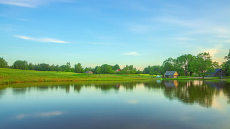 timelapse of picturesque pond nestled amongst lush green fields with overcast clouds gently drifting by, illuminated by changing light and colours
