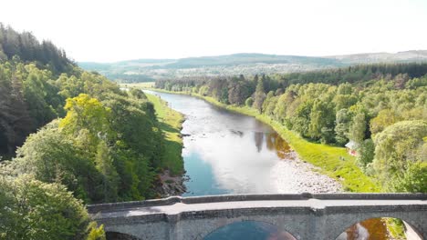 Puente-De-Piedra-A-Través-Del-Río-En-La-Naturaleza-De-Las-Tierras-Altas-De-Escocia,-Soleado,-Drone