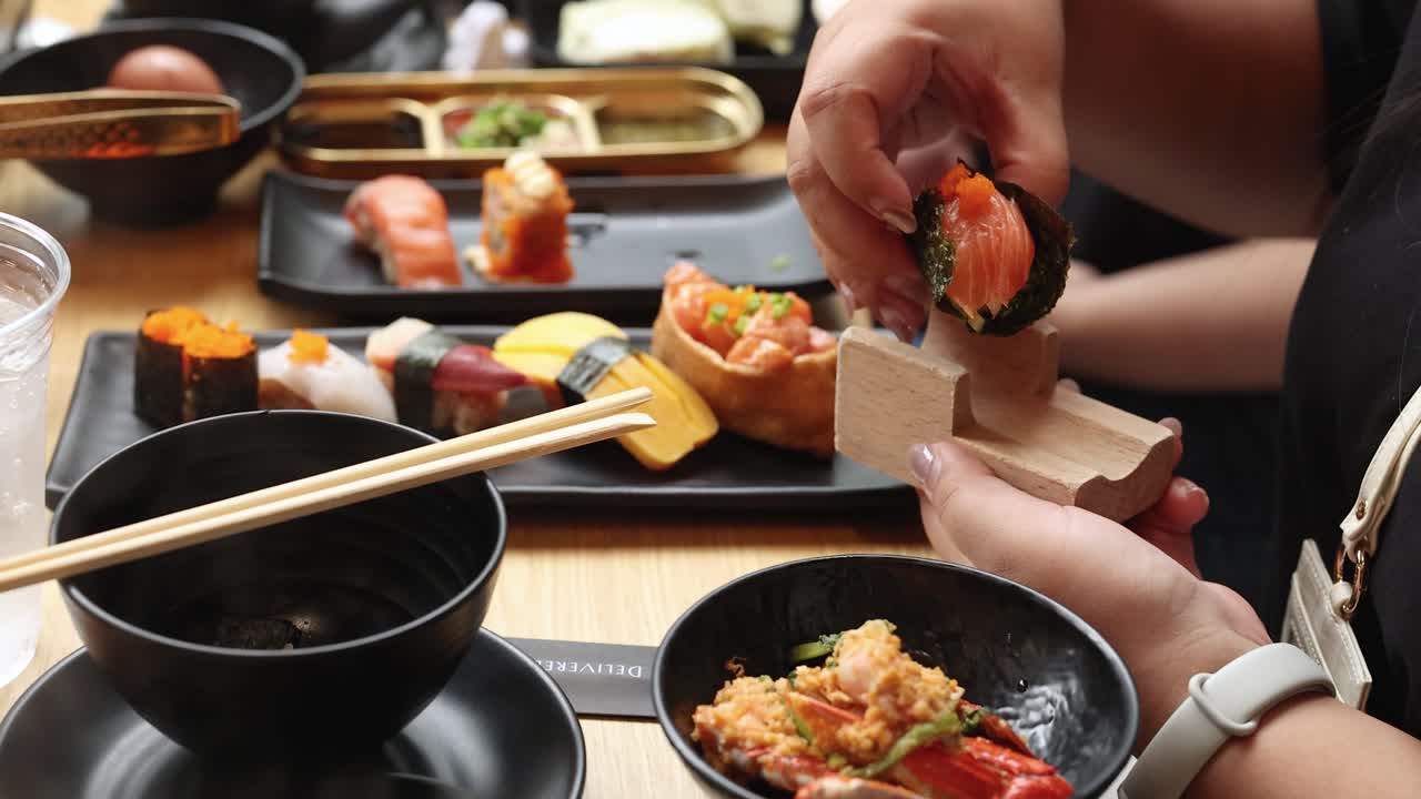 Person arranges assorted sushi nigiri on wooden block, bright natural lighting, close-up perspective