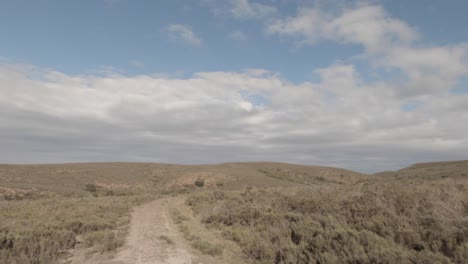 POV-driving-through-dry,-rolling-African-savanna-on-tiny-dirt-road