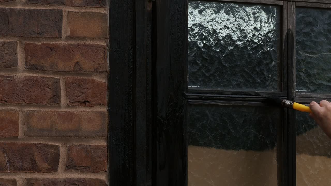 Woman’s hand painting a garage door with wood preservative