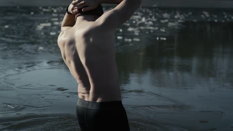 caucasian adult man slowly getting into a frozen lake from the pier in the winter.