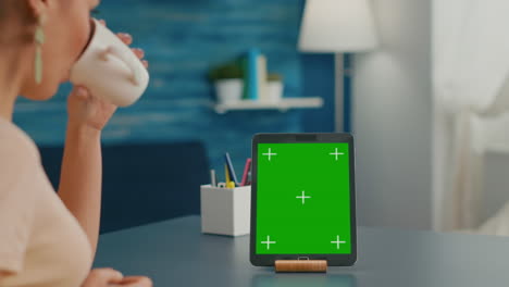 Woman-drinking-a-cup-of-coffee-while-looking-at-tablet-computer