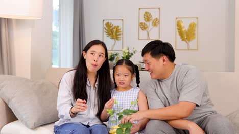 a family of three sits on a sofa, watching tv and eating popcorn in a cozy living room