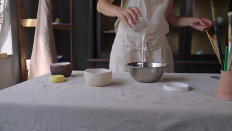 woman pouring liquid onto ceramic bowl in pottery studio