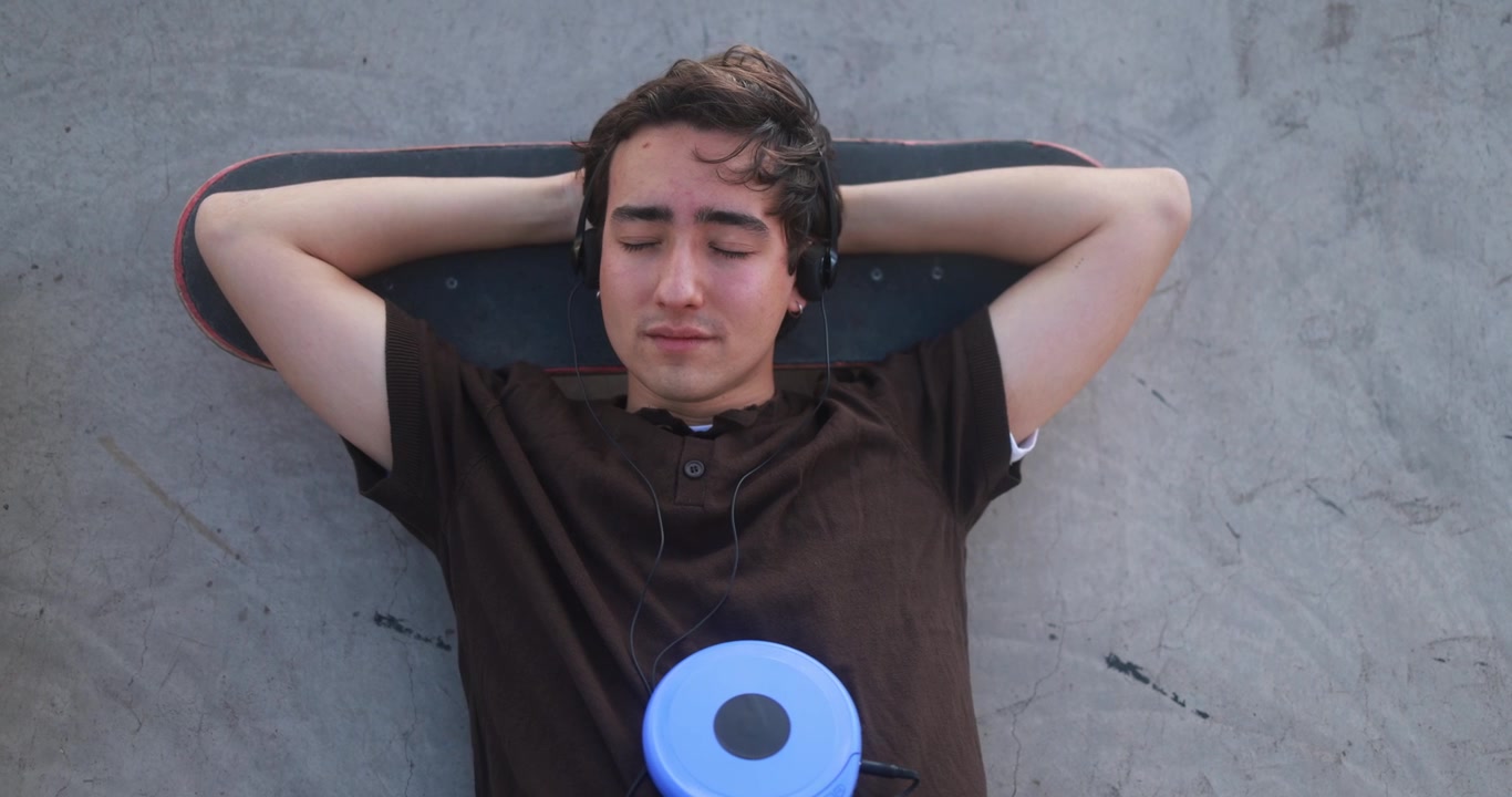 Jonge man ontspannen op zijn skateboard luisterend naar muziek met een cd-speler