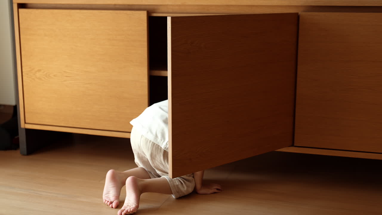 Unrecognized toddler boy opens a wooden chest in the room. Little kid sneaks inside the piece of furniture to hide