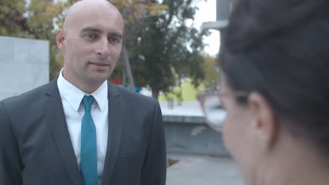 serious businessman meeting with female colleague outside, standing and listening to her