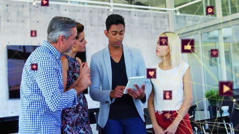 Animation-of-globes-of-digital-icons-against-diverse-colleagues-discussing-over-tablet-at-office