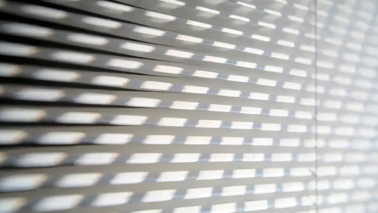 Sunlight shifting through slats, band sliding across pale wall in room, with vertical cord