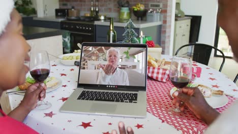 una pareja afroamericana con vino usando una computadora portátil para una videollamada de navidad con una mujer feliz en la pantalla