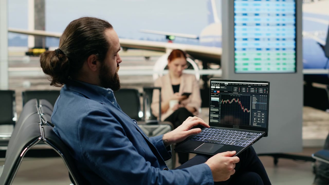 Businessman reviewing stock market graphs on laptop in airport lounge